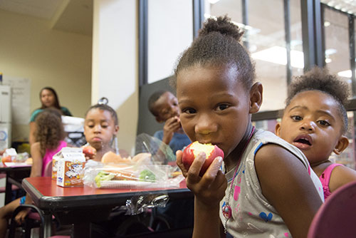 A group of kids sitting at a table mug for the camera as they eat snacks.