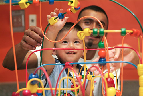 A father and young child play with a bead maze.