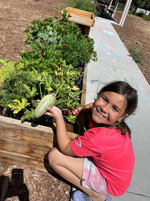 Photo of a girl smiling next to a raised garden bed.