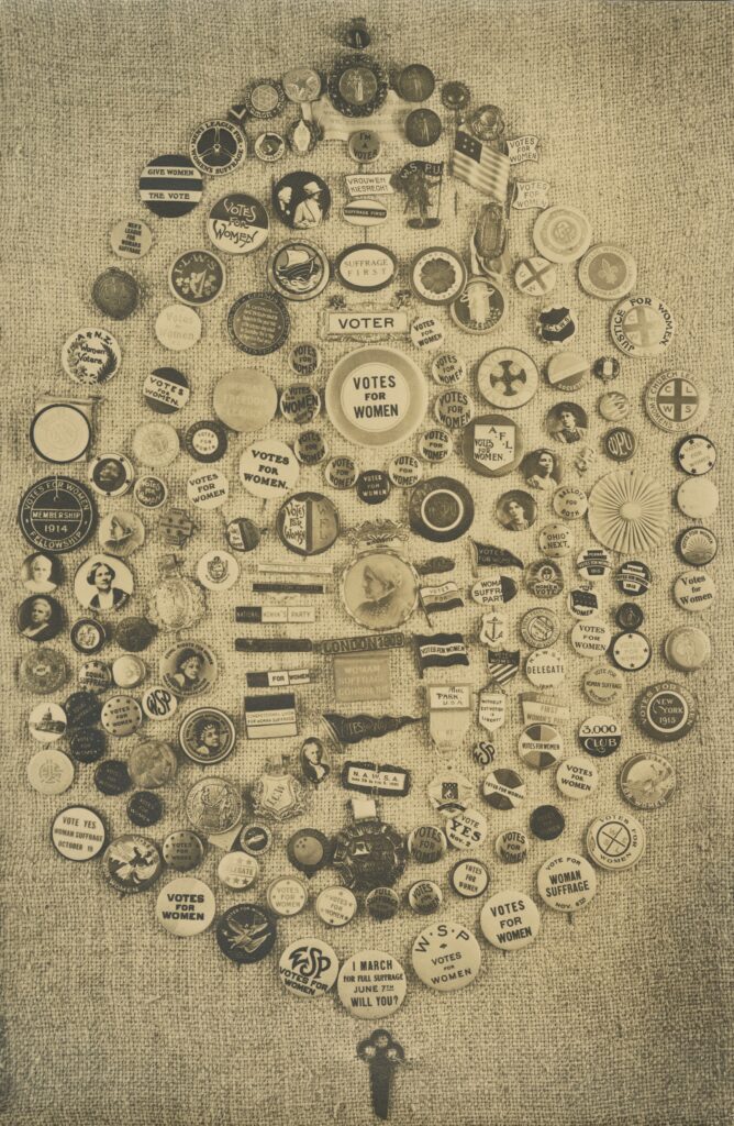 A collection of women’s suffrage buttons displayed on a cloth background.