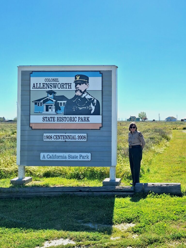 A person standing next to a sign that reads "Colonel Allensworth State History Park 1908 Centennial 2008 A California State Park".