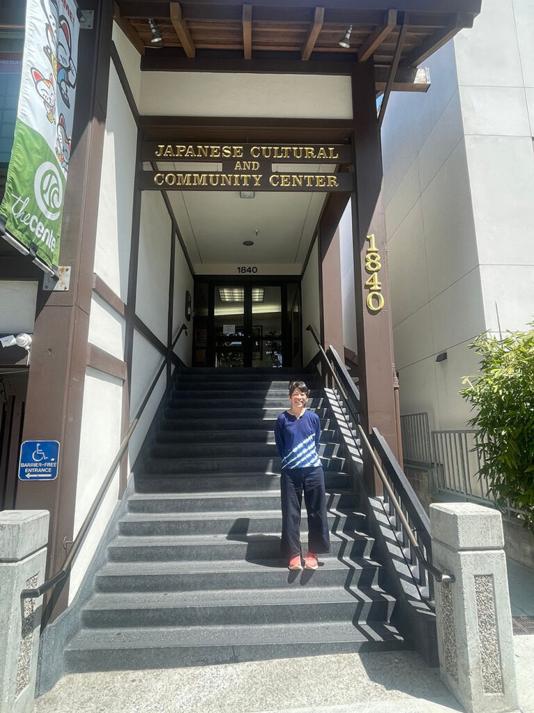A person standing on the steps of a building with a sign overhead that reads "Japanese Cultural and Community Center".