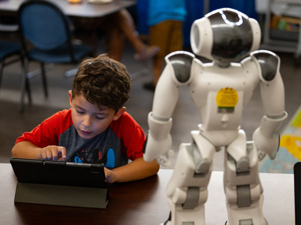 A child uses a tablet to talk with a NAO robot for social interaction.