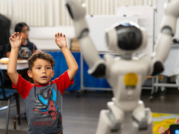 A child mirrors the motions of the NAO robot for social interaction by putting their hands up in the air.