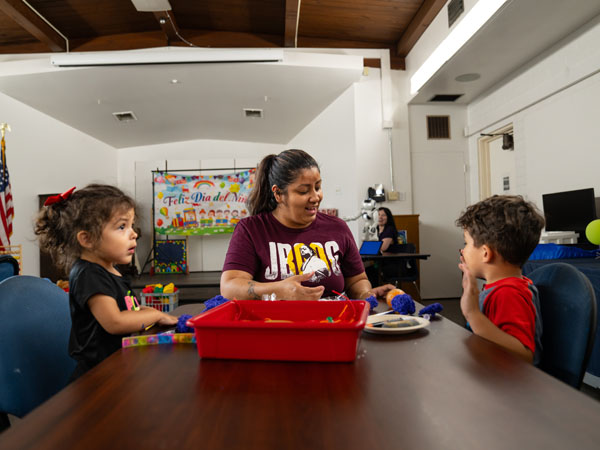 An adult leads two children through a craft.