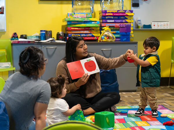 A female library staff member shows book and toy to young child.