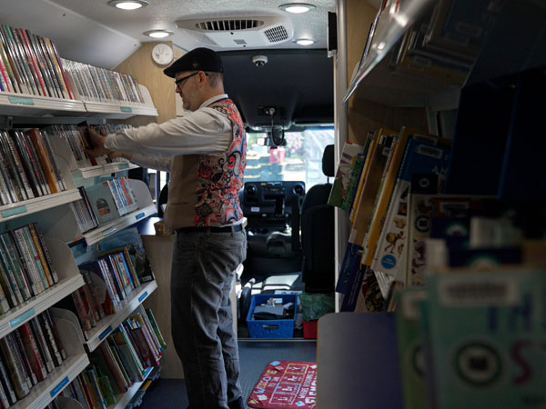 A library worker checks out materials to a family of three at a bookmobile stop.