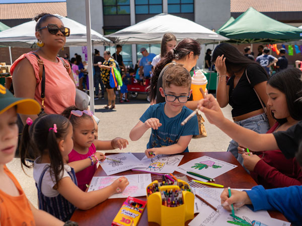 A group of children and families sit around a table with art supplies coloring.