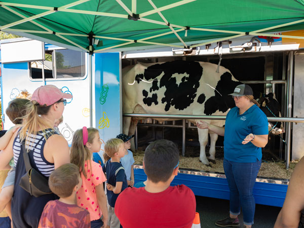 A dairy farmer stands and lectures in front of black and white cow while families listen.