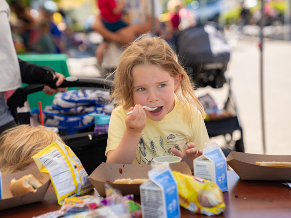 A young girl taking a bite from a fruit cup with a spoon.