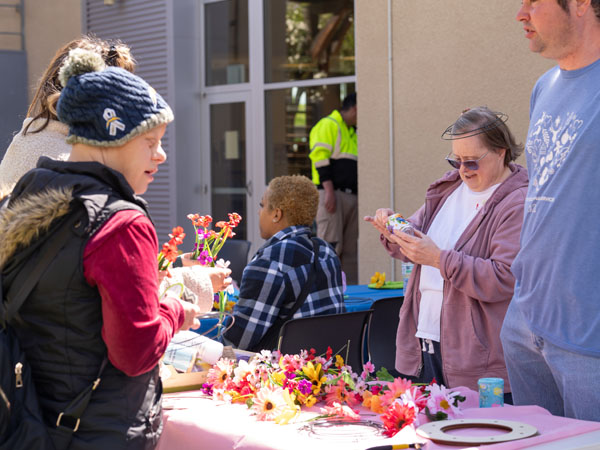 An outdoor table covered with paper flowers, and people standing around it.