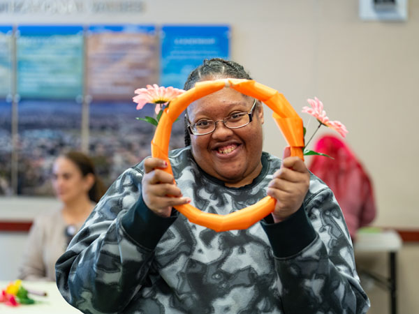 Woman smiling and holding up an orange ribbon covered wreath framing her face.