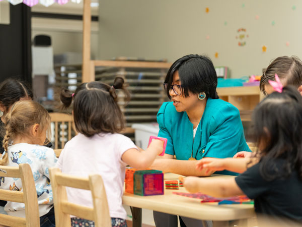 A library worker sits a table with young children working with crafting materials together.