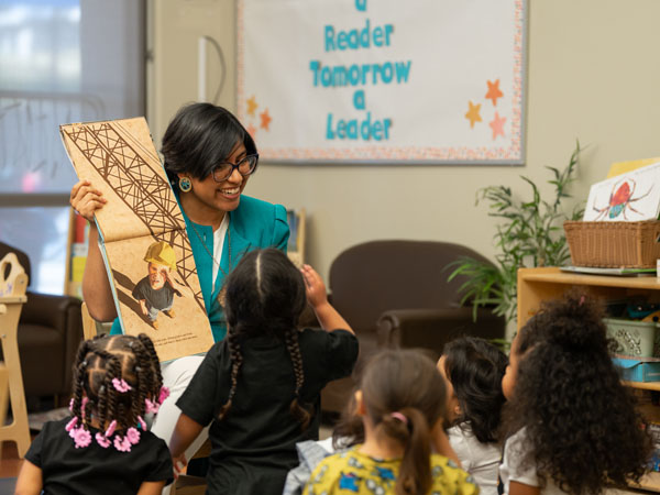 A library worker displays a book to young children in a classroom storytime environment.