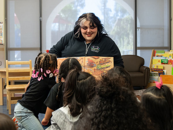 A library worker displays a book to young children in a classroom storytime environment.