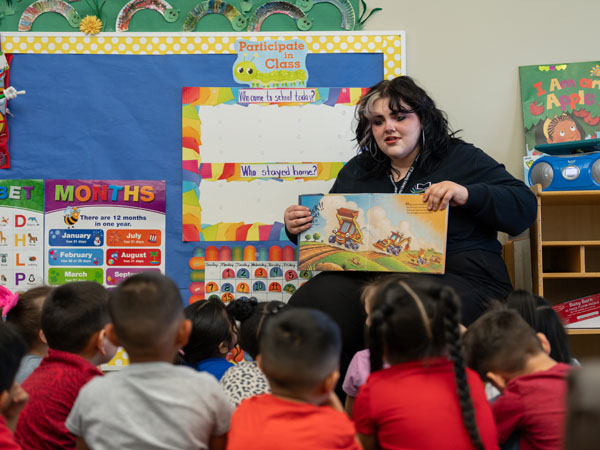 A library worker displays a book to young children in a classroom storytime environment.