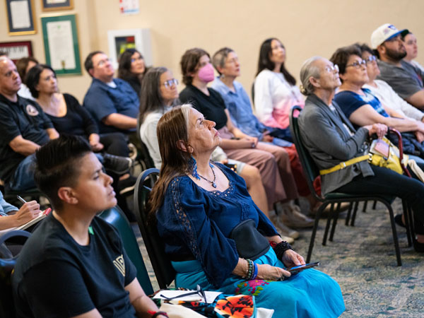 Three rows of seated adults of varied ages, listen to a speaker, not pictured. 