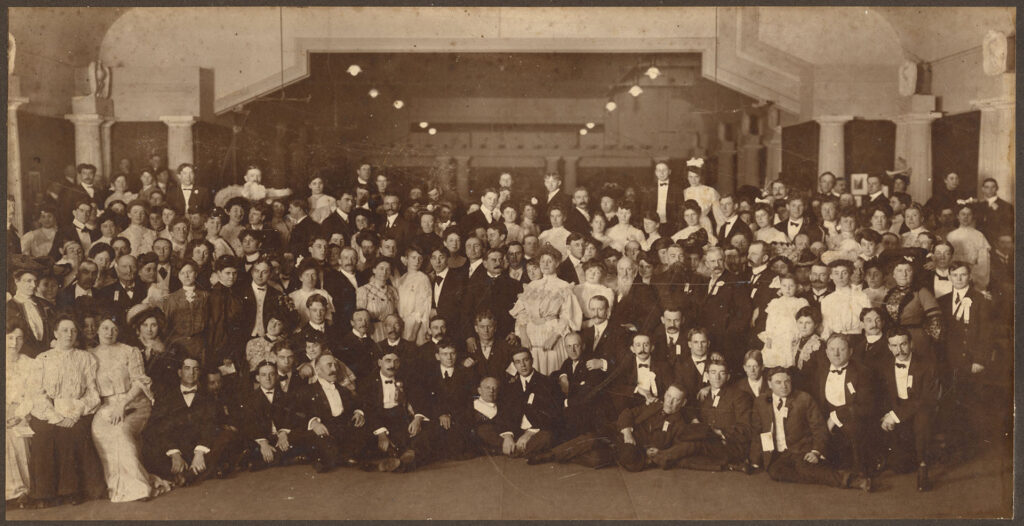 Black and white group portrait of approximately two hundred men and women in a ballroom dressed in formal attire.