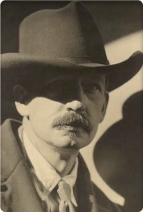 Sepia photo of a man with a mustache wearing a hat and suit.