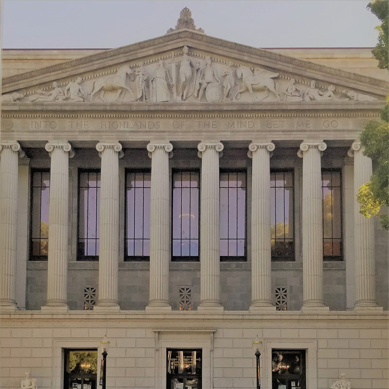 Photo of the exterior of a building with Roman-style columns and a sculpted mural over tall windows.