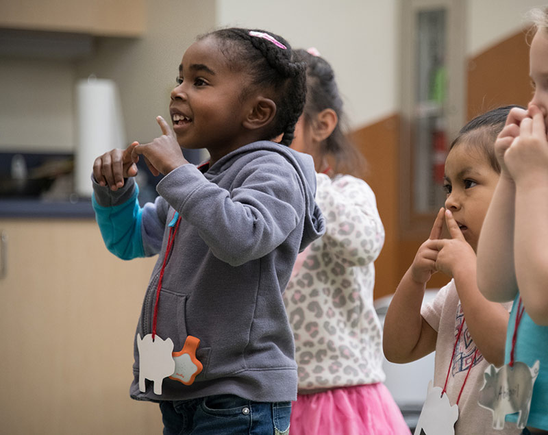 A group of kids stand together and make hand motions.