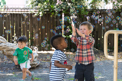 Three small children playing with bubbles in a playground.