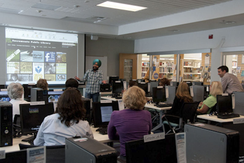 Group of adults in a library computer lab participating in a technology presentation given by staff or a volunteer. Photo Credit The Get Involved Project.