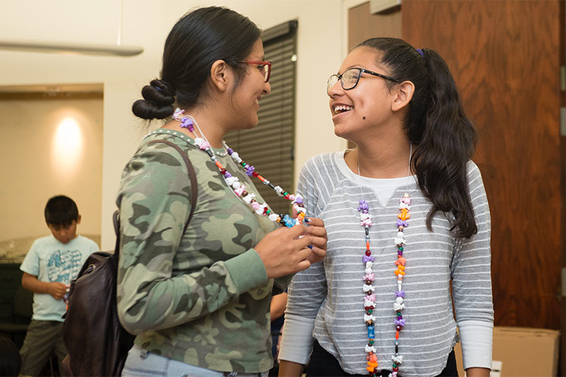 Two teen girls smiling and laughing wearing crafted necklaces. Photo credit Becky Ruppel.