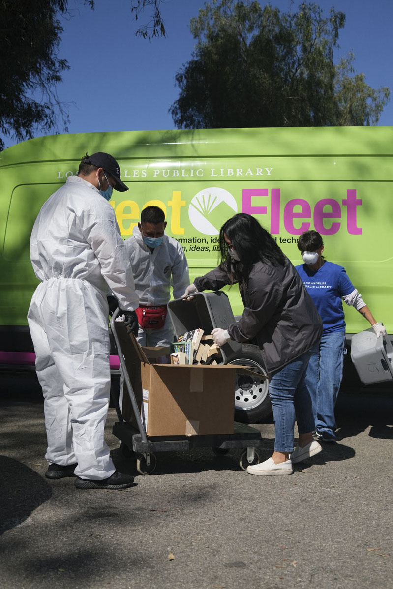 Library staff in PPE transfer donated books into a box for donation in front of their bright green street fleet van. Photo Courtesy of the Los Angeles Public Library.