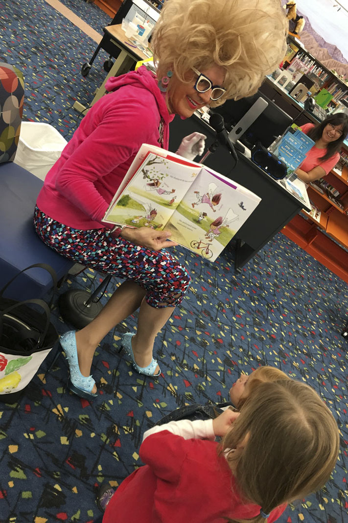 Drag queen seated on a chair reading a story to two children. Photo courtesy Palm Springs Public Library.