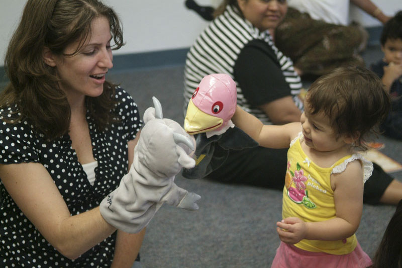 Woman holding puppet plays with a toddler girl holding a blow-up bird head. Photo copyright Terry Lorant.