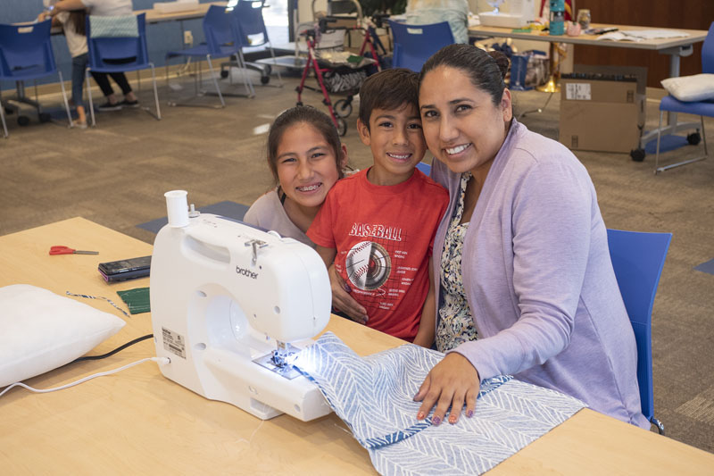 Adult woman, female child, and male child using a sewing machine at their library. Photo courtesy Placentia Library District.