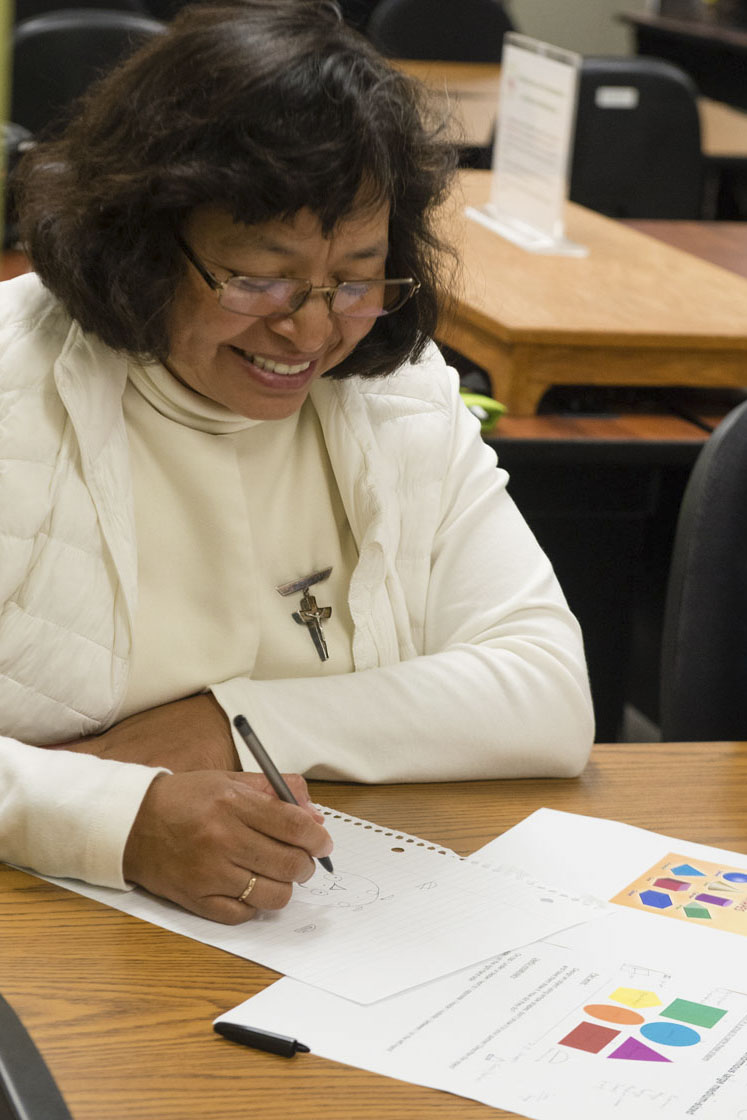 Adult woman smiles while sitting at a table and completing a worksheet. Photo credit Becky Ruppel.