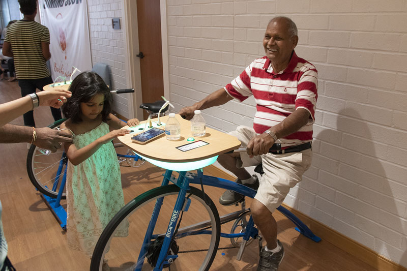 Man riding a stationary bike, with a young girl watching, in his library. Courtesy Placentia Library District.