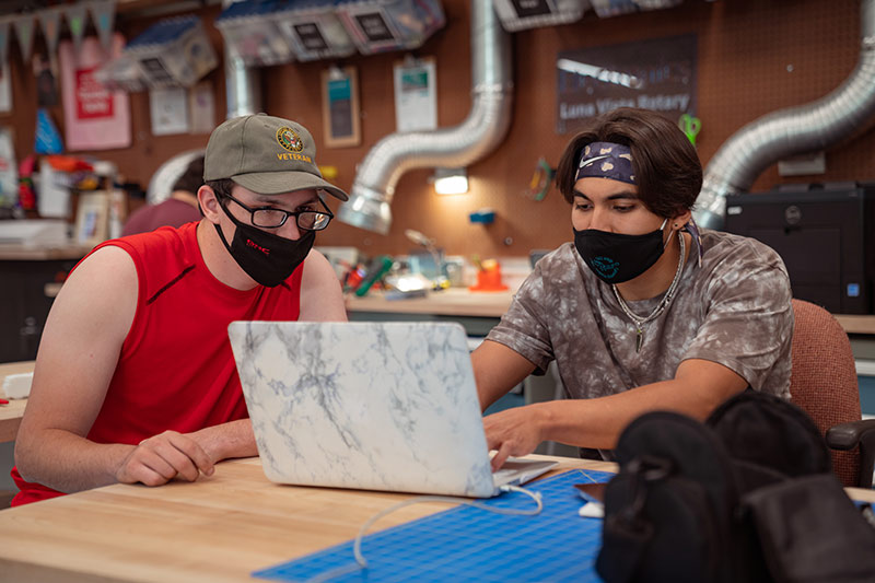 Two young adult men in a makerspace sitting at a table and working together on a laptop. Photo credit Christian Koszka.