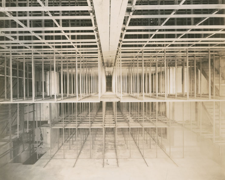 Black and white photo of a three-story framework apparently under construction inside a large room.