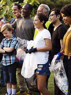 A group of volunteers, all ages, standing together in an outdoor setting, smiling.