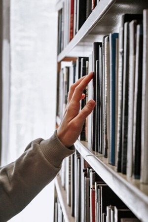 Photo of hand reaching toward books on a library shelf.